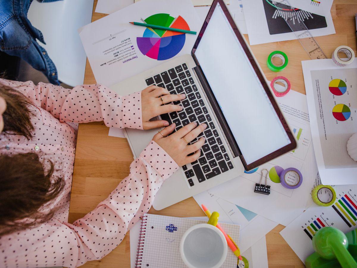 Persona trabajando en una laptop sobre un escritorio con gráficos y material de diseño
